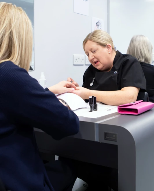 Two beauty therapy students perform nail treatments on clients at a manicure station, engaging in hands-on training in a salon-like environment. Two beauty therapy students perform nail treatments on clients at a manicure station, engaging in hands-on training in a salon-like environment.